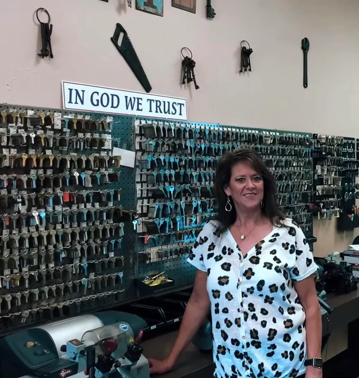 A woman in the Noack Locksmith shop beside key-cutting equipment and an extensive wall of keys.